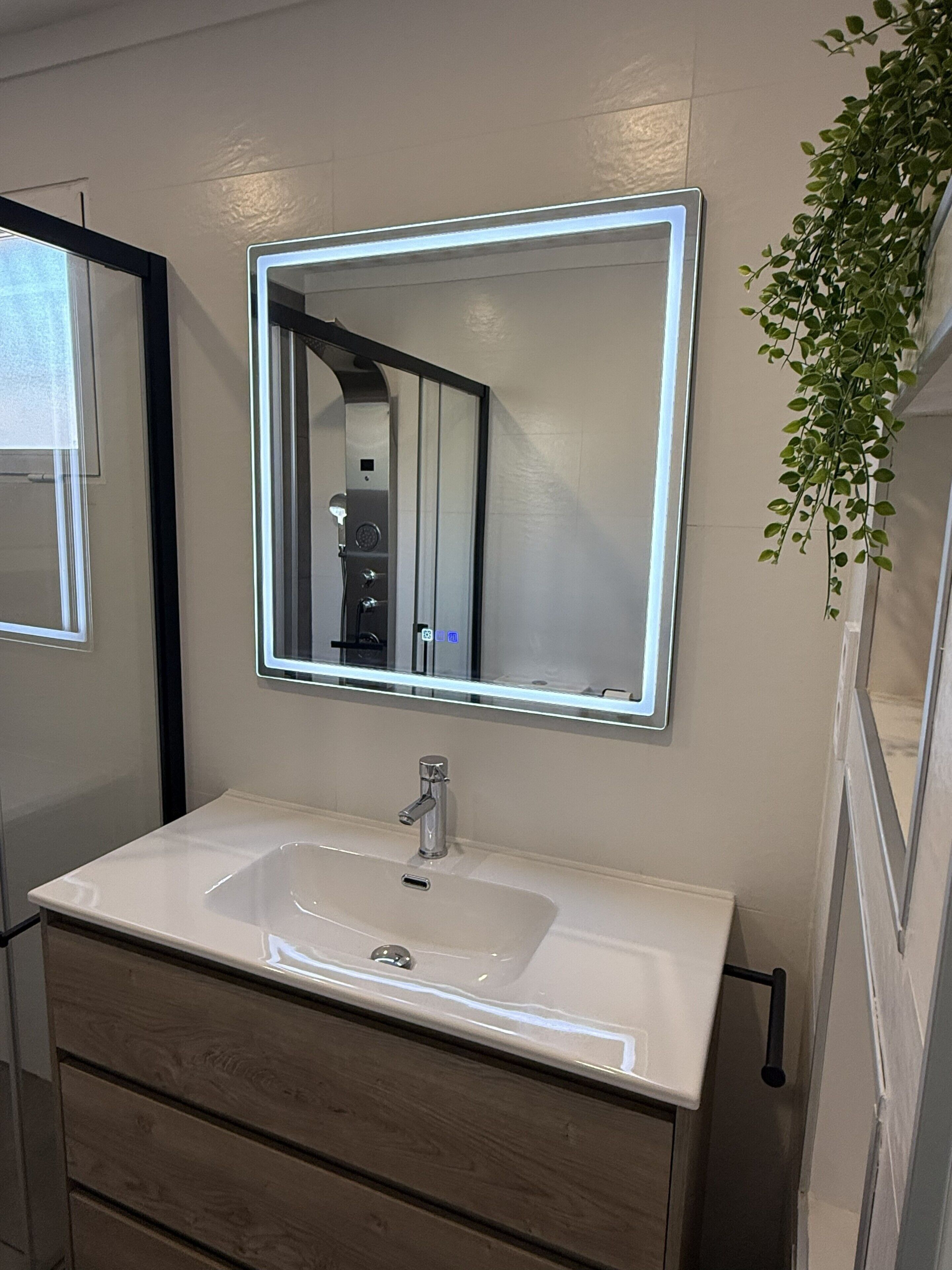 A bathroom with a white sink, a mirror with LED lights, and a potted plant.