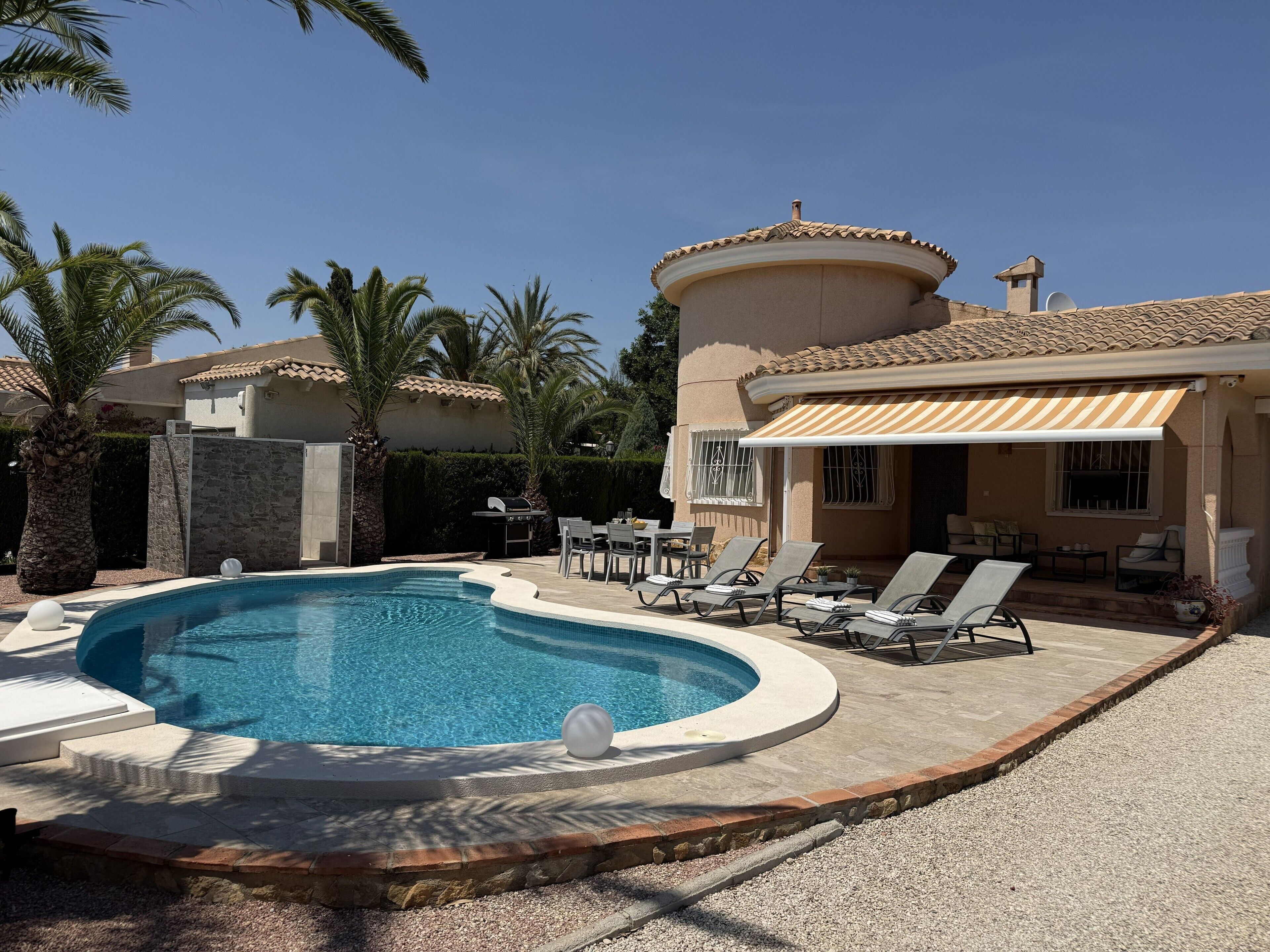 Una piscina con sillas de descanso, zona de barbacoa y terraza cubierta.
