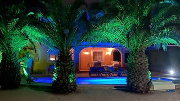 A pool area with palm trees and a building with a covered seating area.