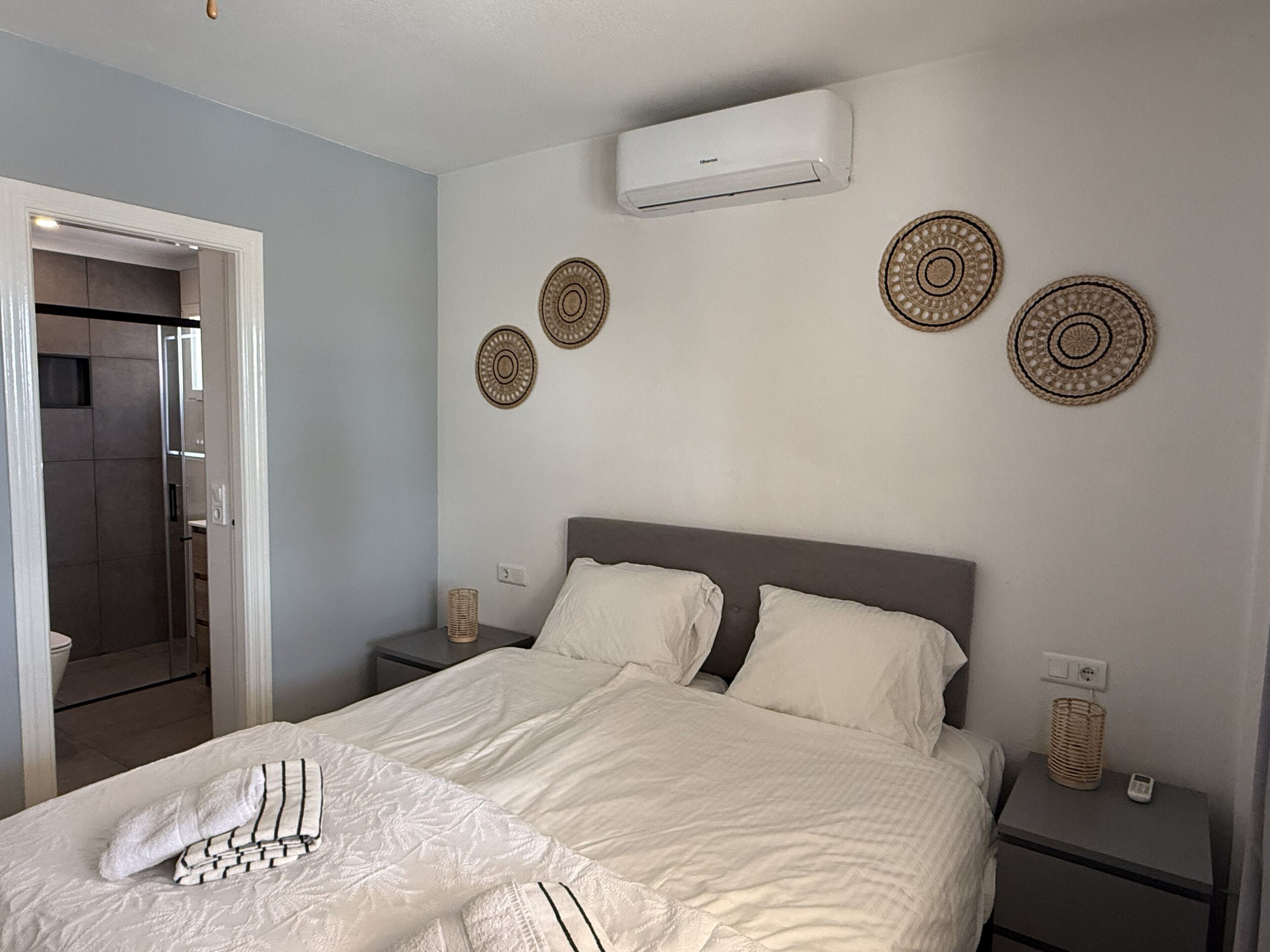 A hotel room with a bed, bedside tables, an air conditioning unit, and decorative wall plates.