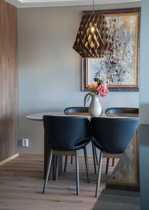 Un comedor con una mesa redonda, sillas negras, un florero con flores y una lámpara colgante.