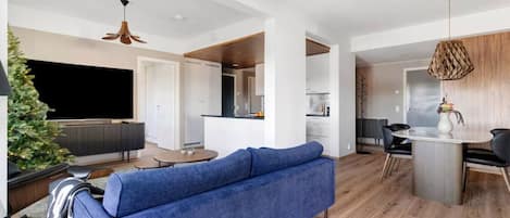 A modern living room with a blue sofa, a dining area with a table and chairs, and a kitchen in the background.