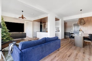 A modern living room with a blue sofa, a dining area with a table and chairs, and a kitchen in the background. - Aurora Sky Penthouse By Lapland Host (Rovaniemi)