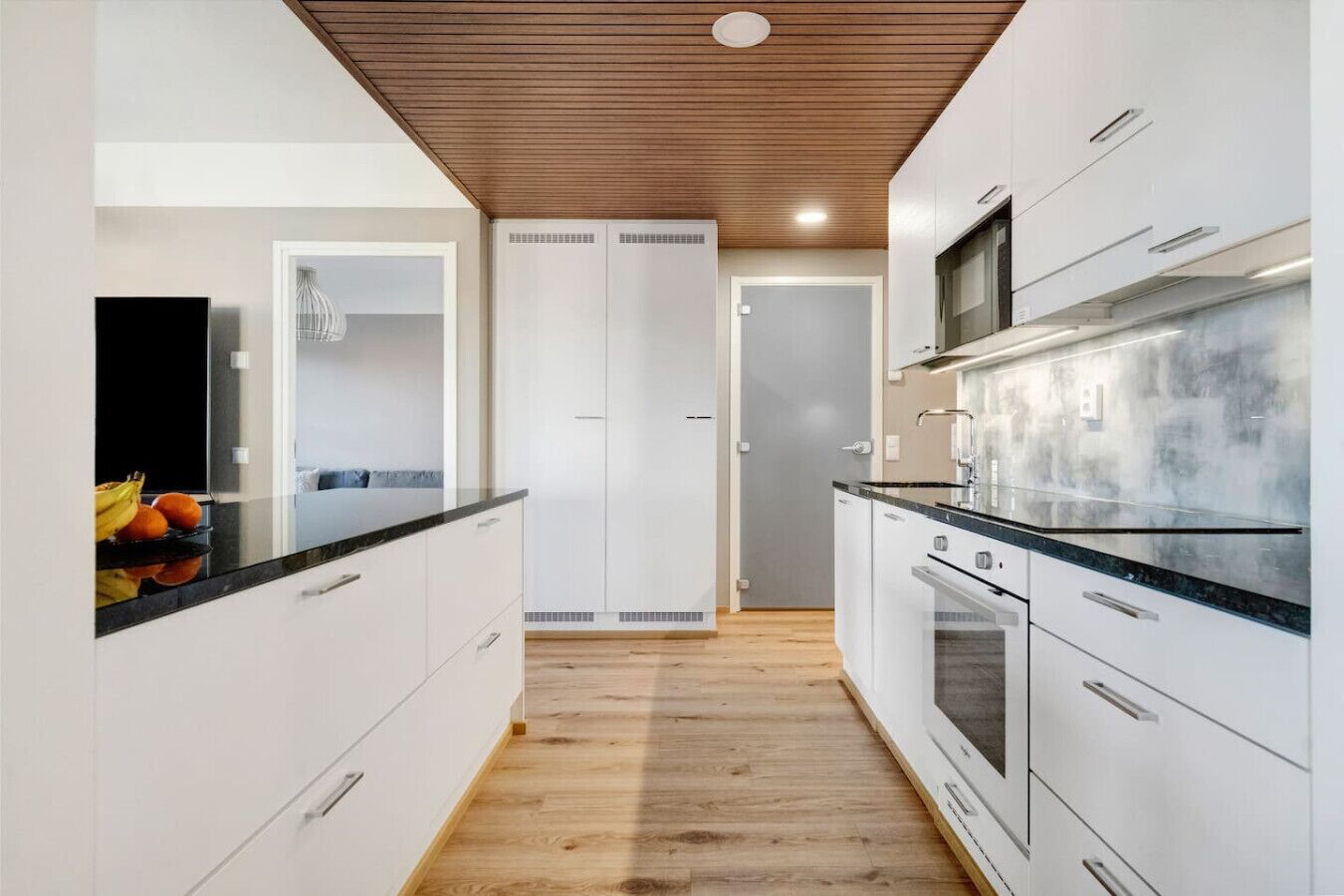 A modern kitchen with white cabinetry, a wooden ceiling, and a black countertop.