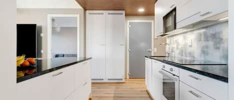 A modern kitchen with white cabinetry, a wooden ceiling, and a black countertop.