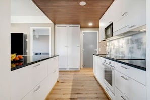 A modern kitchen with white cabinetry, a wooden ceiling, and a black countertop. - Aurora Sky Penthouse By Lapland Host (Rovaniemi)
