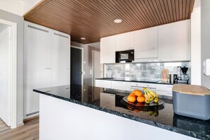 Una cocina moderna con armarios blancos, encimera negra y techo de madera.