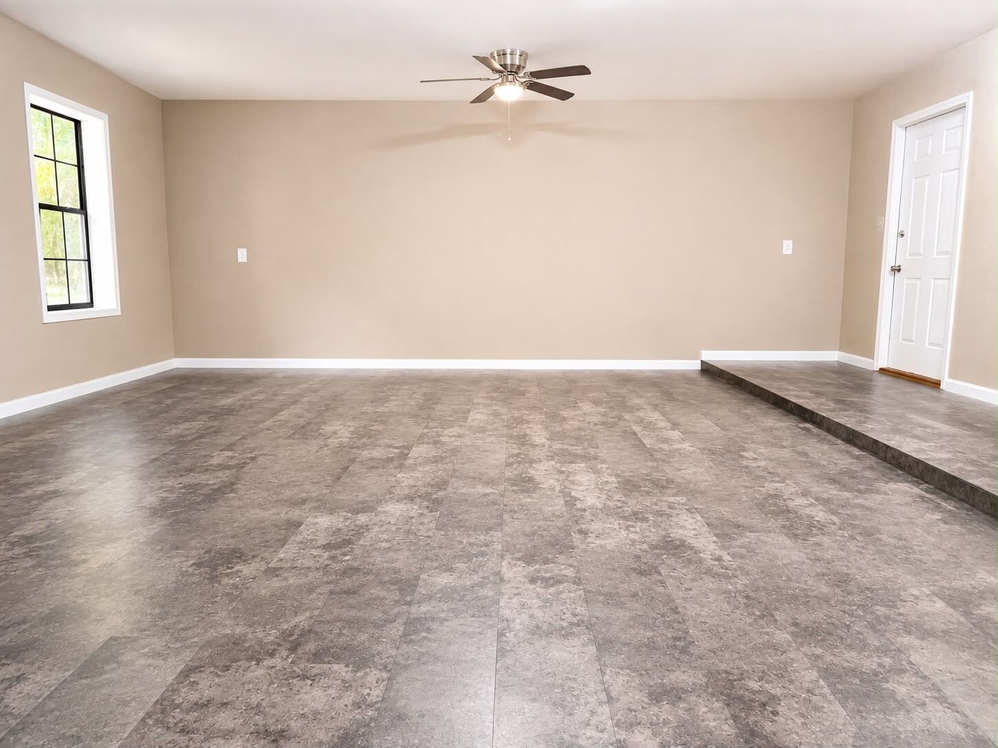 A spacious room with a high ceiling, a ceiling fan, and a large window.