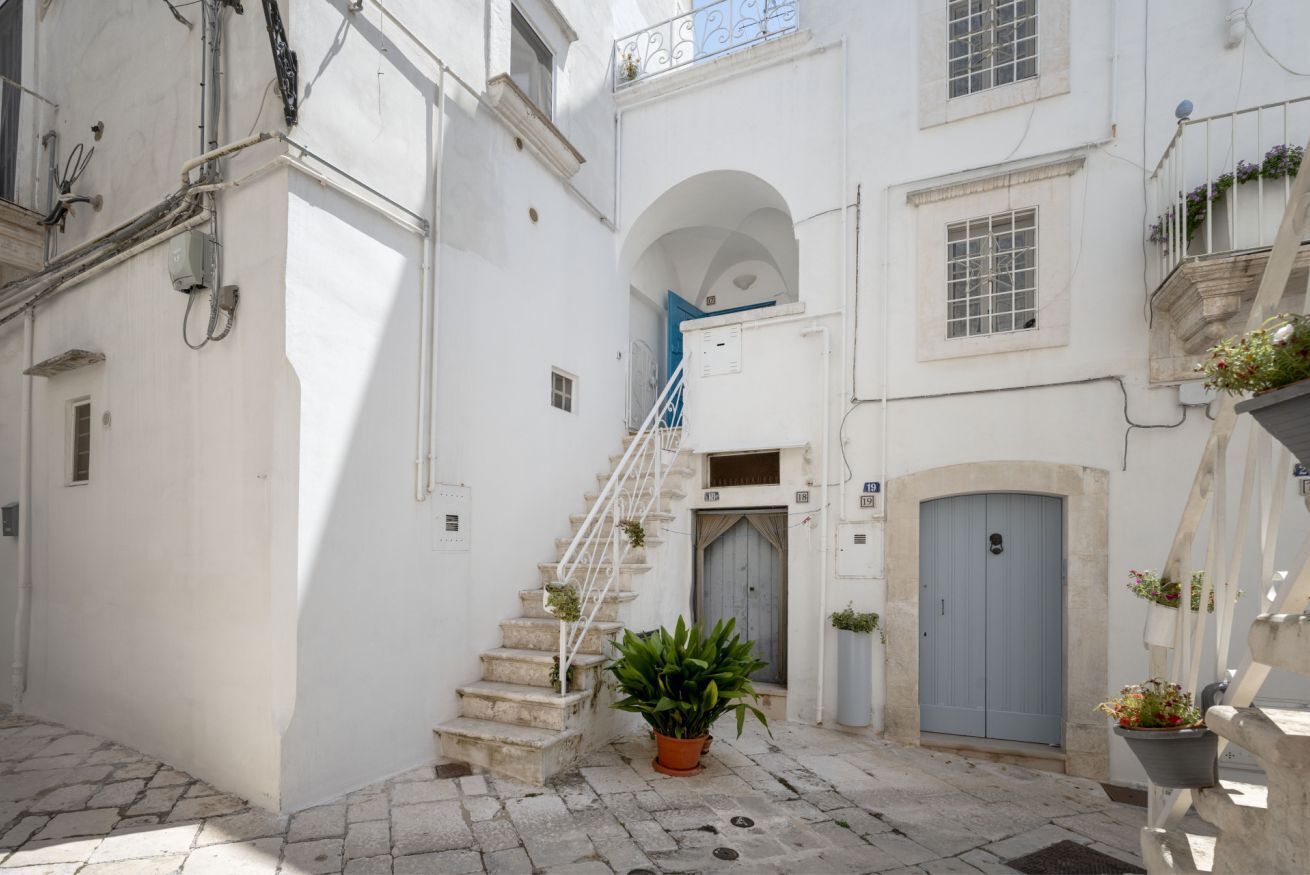 Una calle estrecha con un edificio blanco, una escalera y una planta en maceta.