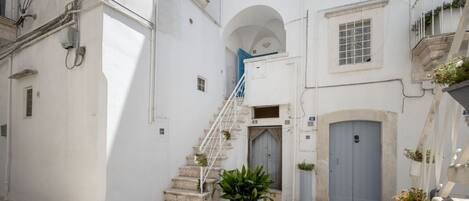 Una calle estrecha con un edificio blanco, una escalera y una planta en maceta.