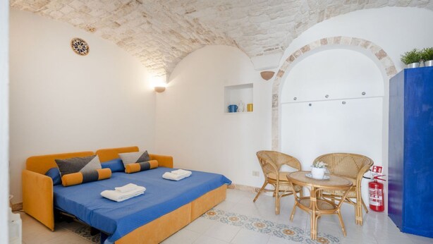 A room with a bed, two chairs, a small table, a fire extinguisher, and a decorative wall piece. - A cozy 48-square-meter apartment, ideal for two people, located on the first floor of a typical historic center home (accessible via stairs). The location is perfect: the property is right in the town center (within the ZTL/restricted traffic zone), with (Martina Franca)