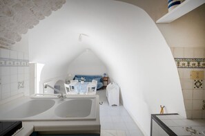 Une pièce compacte comprenant une grande baignoire, un coin repas avec une table et des chaises, et un petit coin salon avec un canapé.