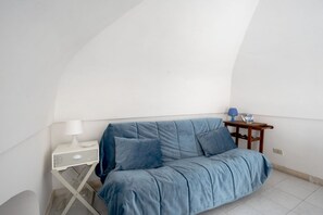 A room with a blue sofa, a small white table with a lamp, and a blue table lamp. - A cozy 48-square-meter apartment, ideal for two people, located on the first floor of a typical historic center home (accessible via stairs). The location is perfect: the property is right in the town center (within the ZTL/restricted traffic zone), with (Martina Franca)