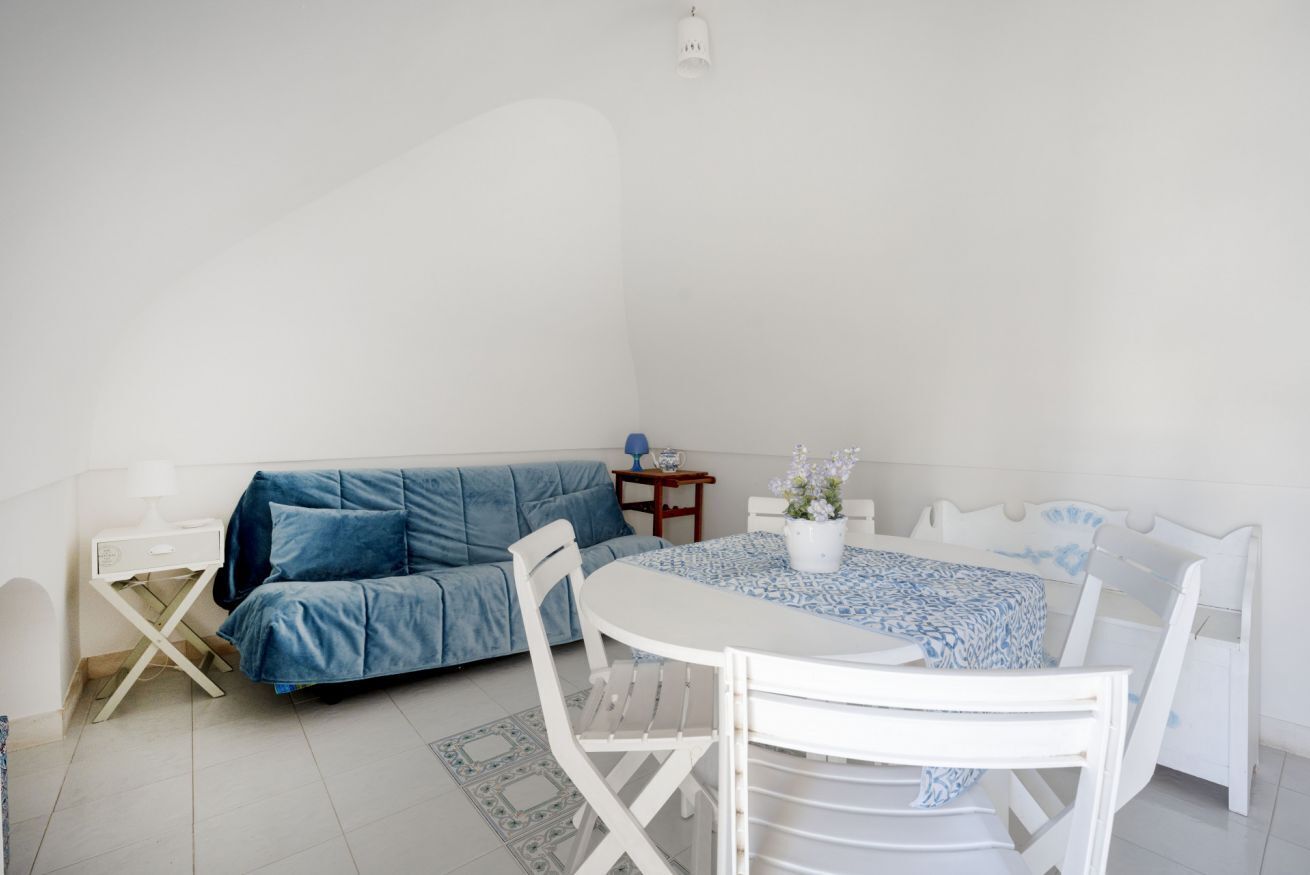 Ein Zimmer mit einem weißen Sofa, einem weißen Esstisch mit Stühlen, einem kleinen Beistelltisch und einer wandmontierten Lampe.