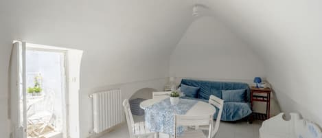 A room with a white table, chairs, a blue sofa, and a small side table with a lamp.