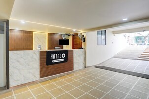 Zona de recepción de hotel con un mostrador de mármol, pared revestida de madera, televisor de pantalla plana y un cartel que indica que el hotel cuenta con servicios para empresas.