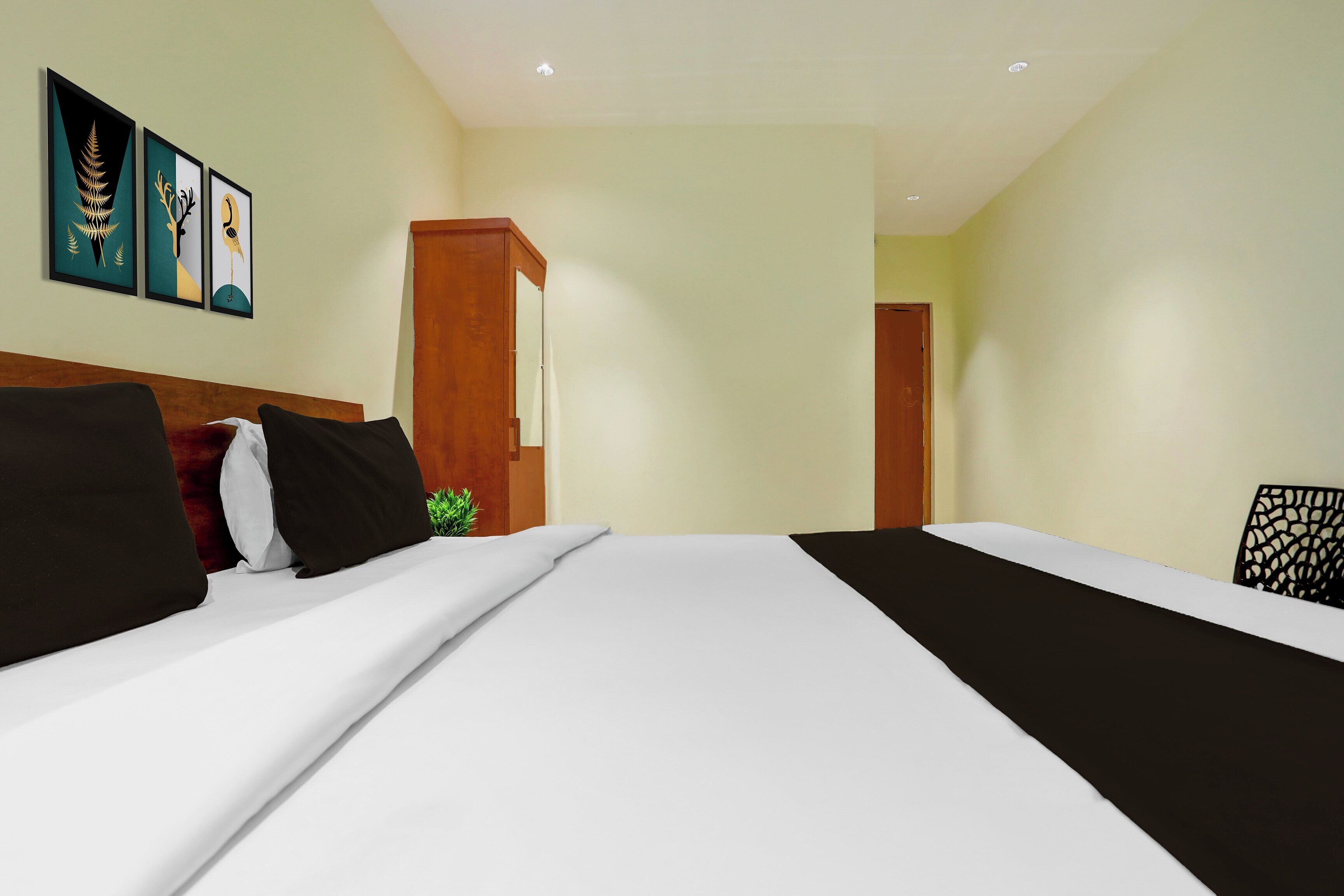 A hotel room with a large bed, a wooden headboard, a small plant, and framed artwork on the wall.