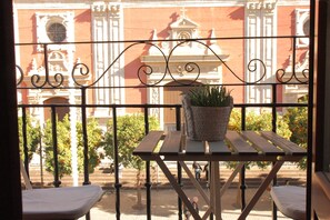 A balcony with a wrought iron railing, a small table with a potted plant, and a view of a building with classical architecture. - Panther Home Salvador (Casco Historico)