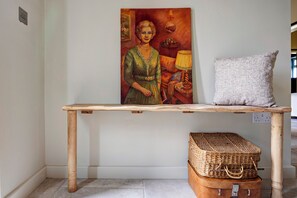 A wooden table with a painting, a textured pillow, and a woven basket on a floor. - Luxury Converted Stable Cottage | Lake District | EV Charger & Private Patio (Carnforth)