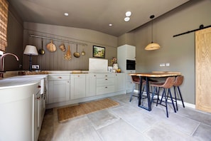 A modern kitchen with white cabinets, a wooden dining table, and a hanging pot rack. - Luxury Converted Stable Cottage | Lake District | EV Charger & Private Patio (Carnforth)