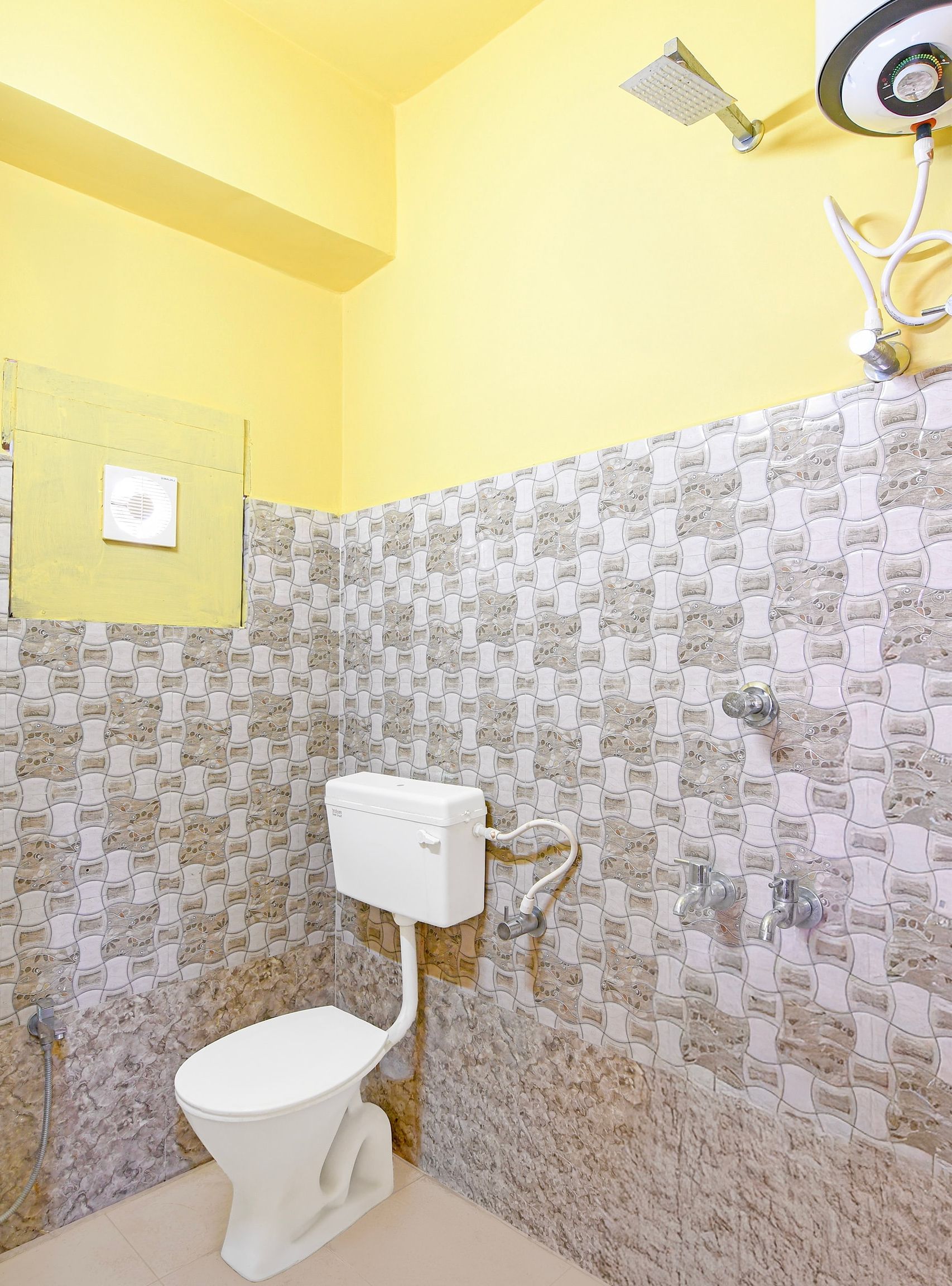 A bathroom with a toilet, a shower, and a wall with a patterned tile design.
