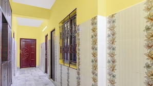 Un pasillo con suelo de baldosas, una puerta roja y una ventana con barrotes.
