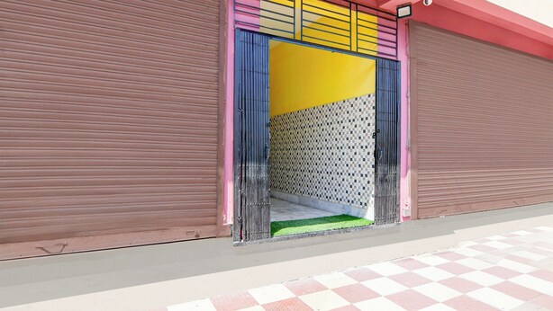 Fachada de edificio con una persiana cerrada, entrada colorida con un muro decorado y suelo a cuadros.
