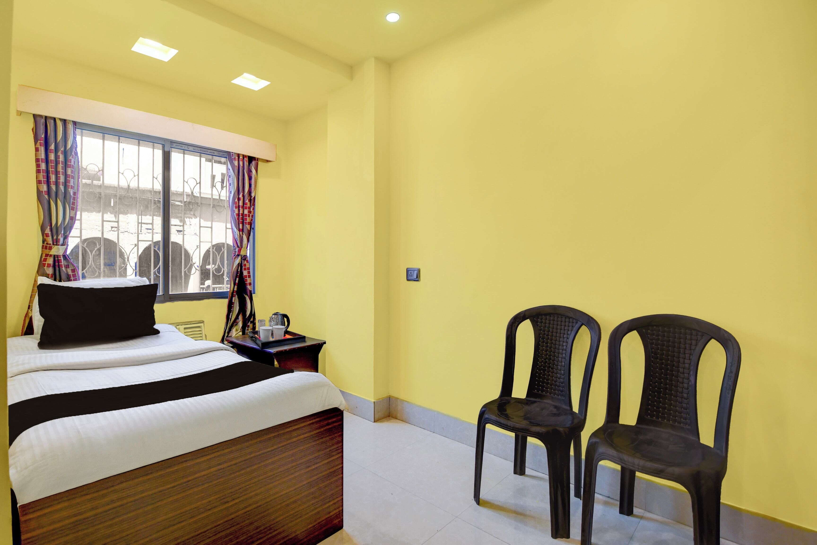 Ein Hotelzimmer mit einem Bett, zwei Stühlen, einem Nachttisch und einem Fenster mit Vorhängen.
