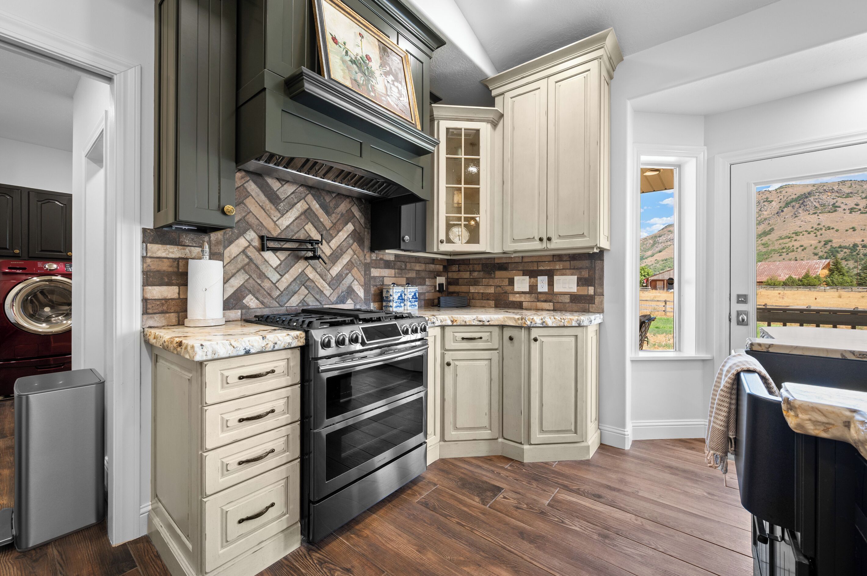Une cuisine avec un dosseret en motif chevron, une cuisinière en acier inoxydable et une grande fenêtre donnant sur un paysage montagneux.