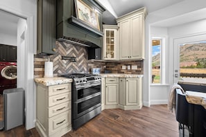 Une cuisine avec un dosseret en motif chevron, une cuisinière en acier inoxydable et une grande fenêtre donnant sur un paysage montagneux.