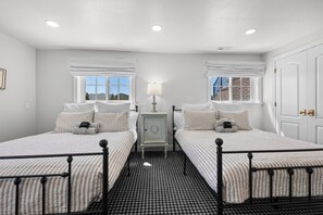 Une chambre double avec deux lits, une table de chevet, une lampe et une vue sur l’extérieur.