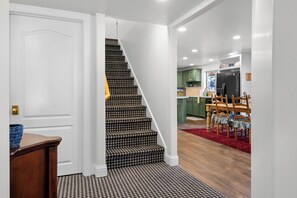Un escalier recouvert d’une moquette à carreaux « pied-de-poule » mène à une cuisine avec des meubles verts et un réfrigérateur noir.