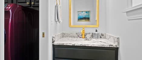 A bathroom with a marble sink, a gold faucet, and a framed painting above the mirror.