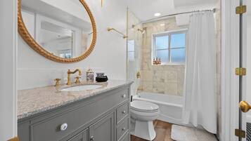 A bathroom with a vanity, sink, mirror, toilet, bathtub, and shower curtain.