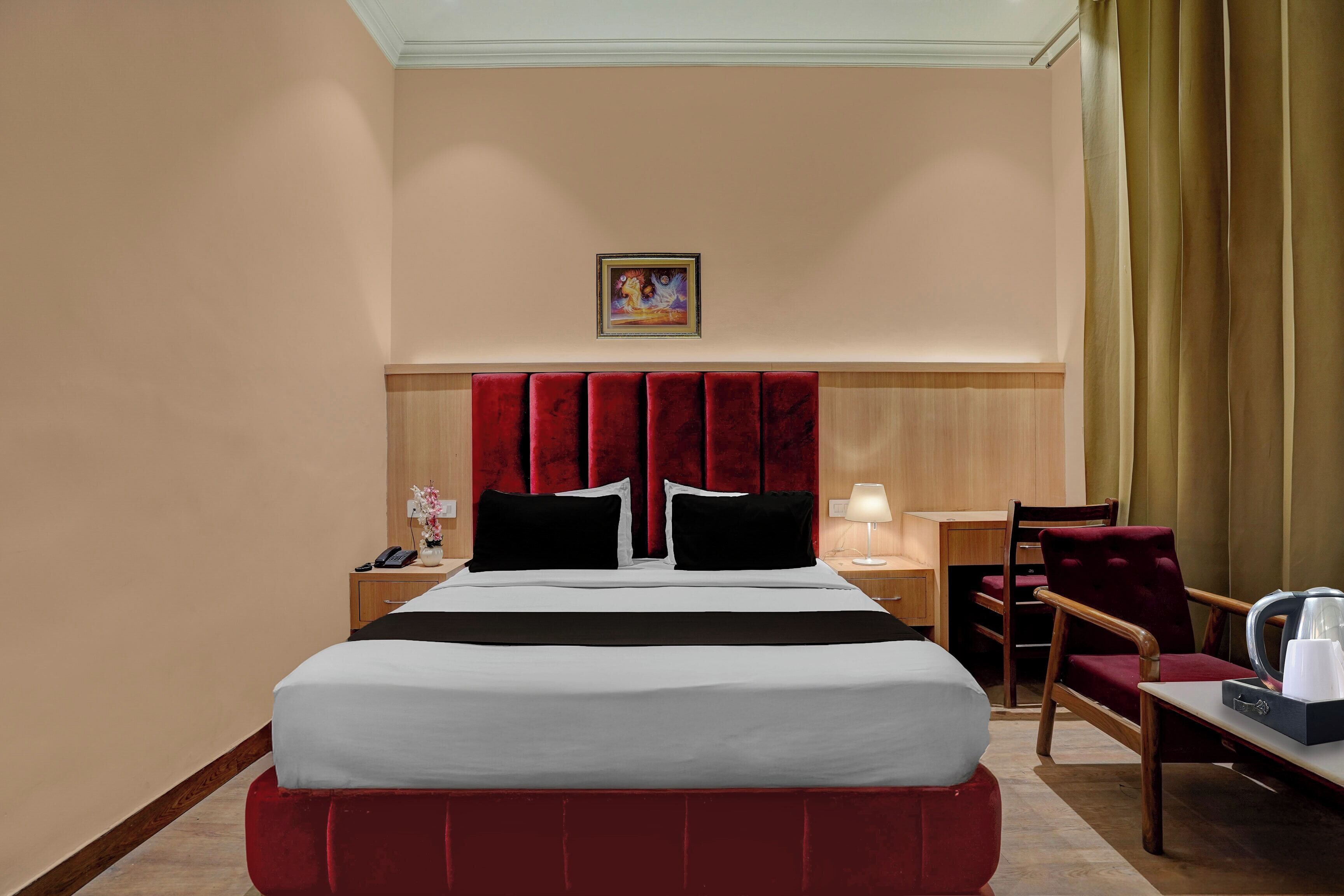A hotel room with a large bed, a desk, a chair, a nightstand, a lamp, and a painting on the wall.