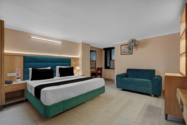 A hotel room with a bed, bedside table, lamp, and a blue sofa.