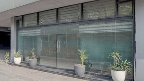 Fachada moderna de edificio con amplios ventanales y plantas en macetas al nivel de la calle.
