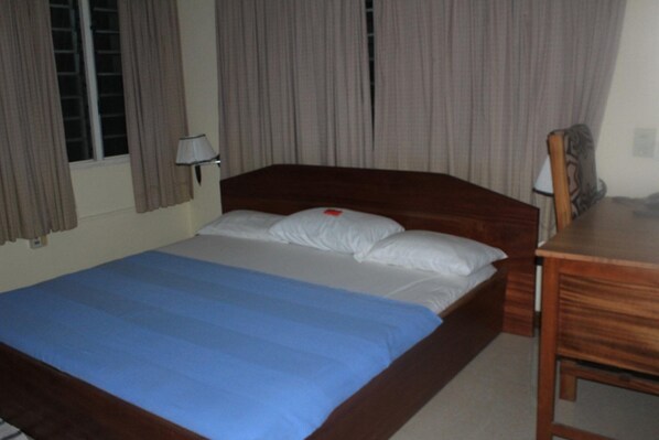 A hotel room with a single bed, a wooden headboard, a desk, and a chair.