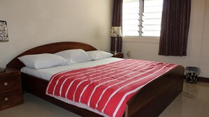 A neatly made bed with a striped blanket, a wooden headboard, a bedside table with a lamp, and a window with curtains. - Loreto Palm Villa: 17 en-suite AC rooms with on-site restaurant (Cape Coast, Ghana)