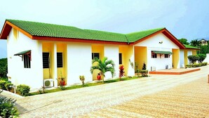 A two-story building with a green roof, multiple windows, and a paved entrance area. - Loreto Palm Villa: 17 en-suite AC rooms with on-site restaurant (Cape Coast, Ghana)