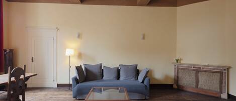 A room with a wooden floor, a sofa, a glass coffee table, a lamp, a door, and a fireplace.