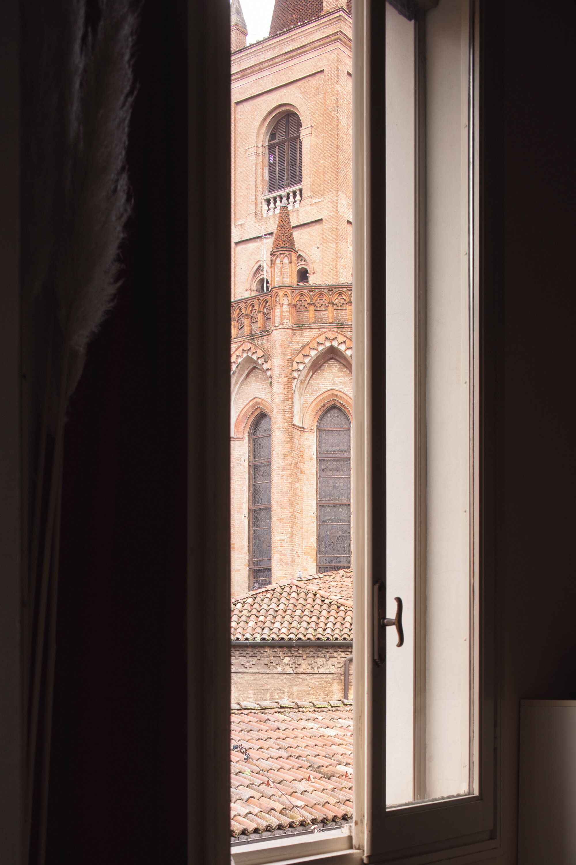 A window with a view of a brick building with arched windows and a tiled roof.