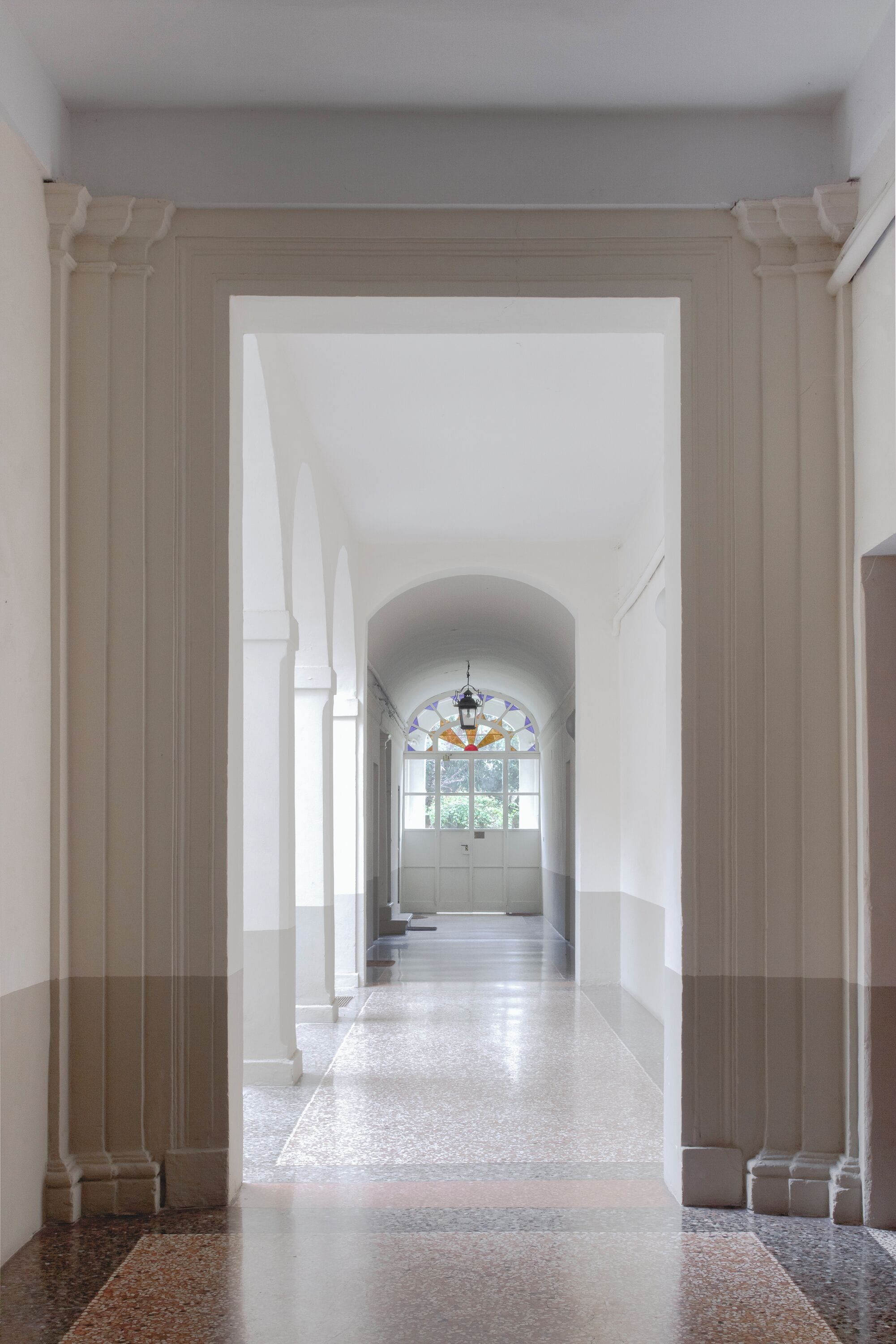 A corridor with a high ceiling, a stained glass window, and a chandelier.
