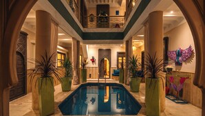 A spacious indoor pool area with a central pool, surrounded by large potted plants, and a balcony overlooking the space. - Riad Chouïa-Chouïa (Marrakech)