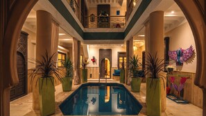 Un vaste espace intérieur abritant une piscine centrale, entourée de grands pots de plantes et donnant sur un balcon qui surplombe l’ensemble.