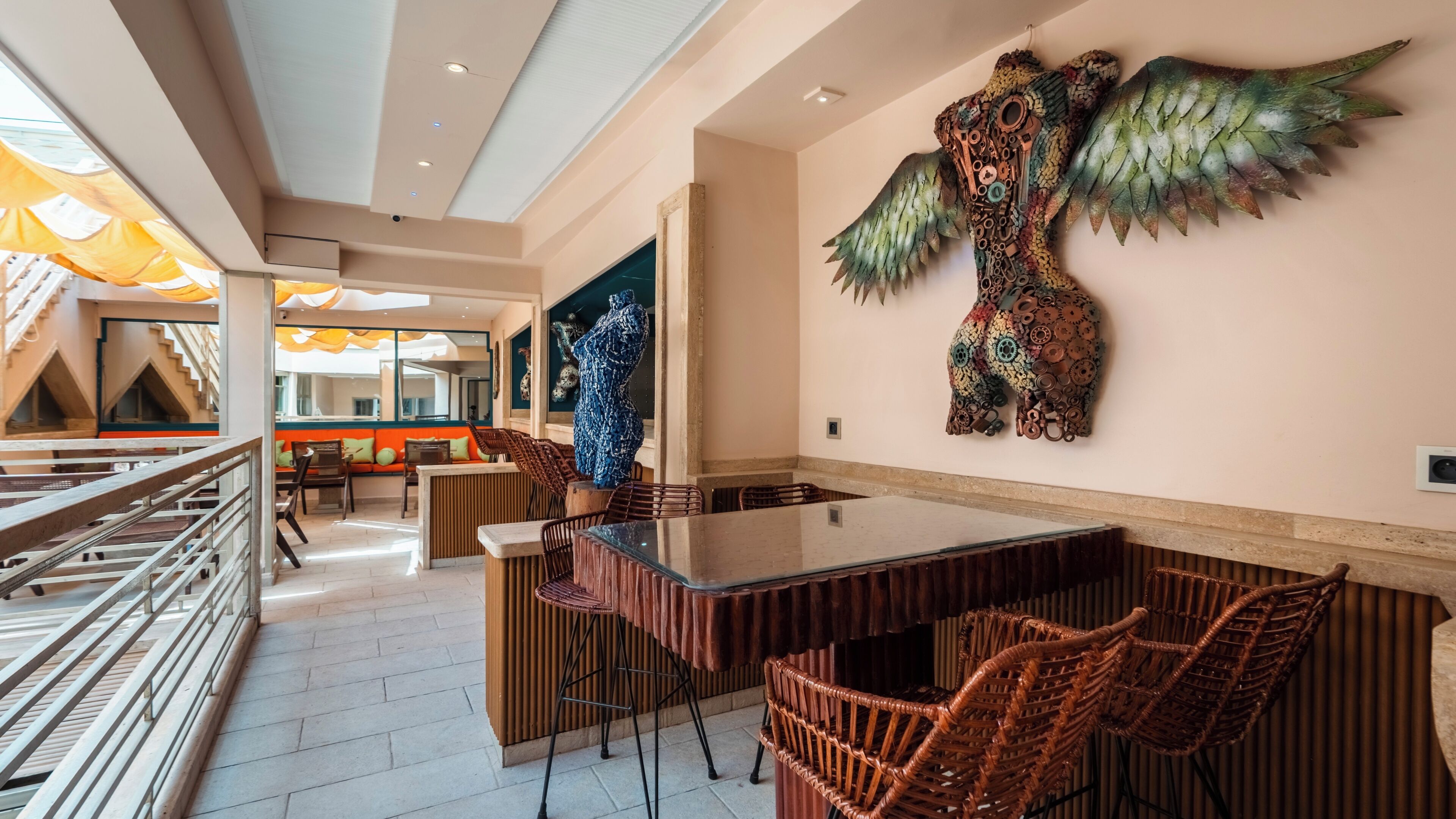 A modern dining area with a glass table and wicker chairs, a large decorative wall piece, and a view of the outdoor area.