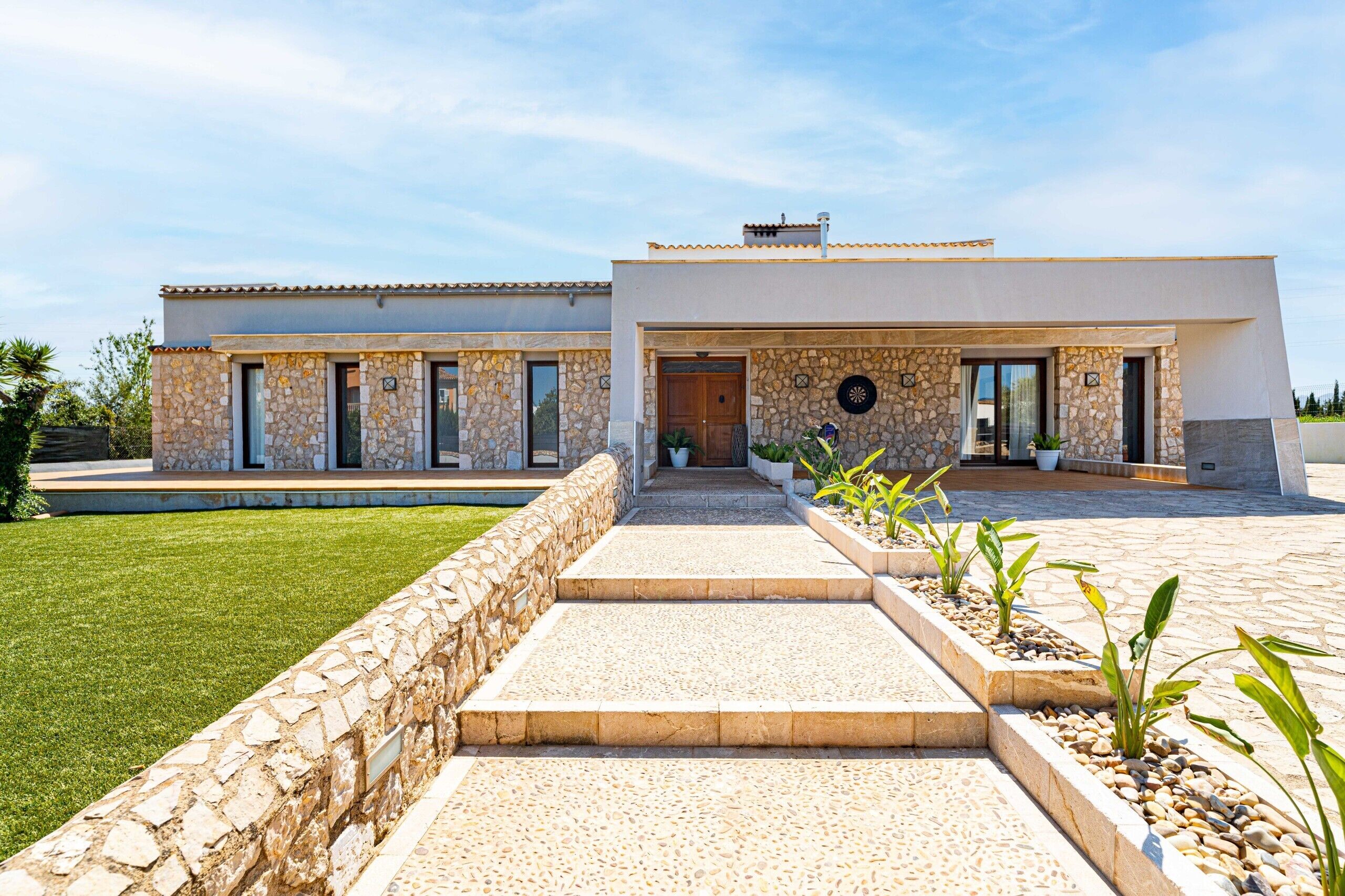 A modern two-story house with a stone facade, a paved driveway, and a well-maintained lawn.