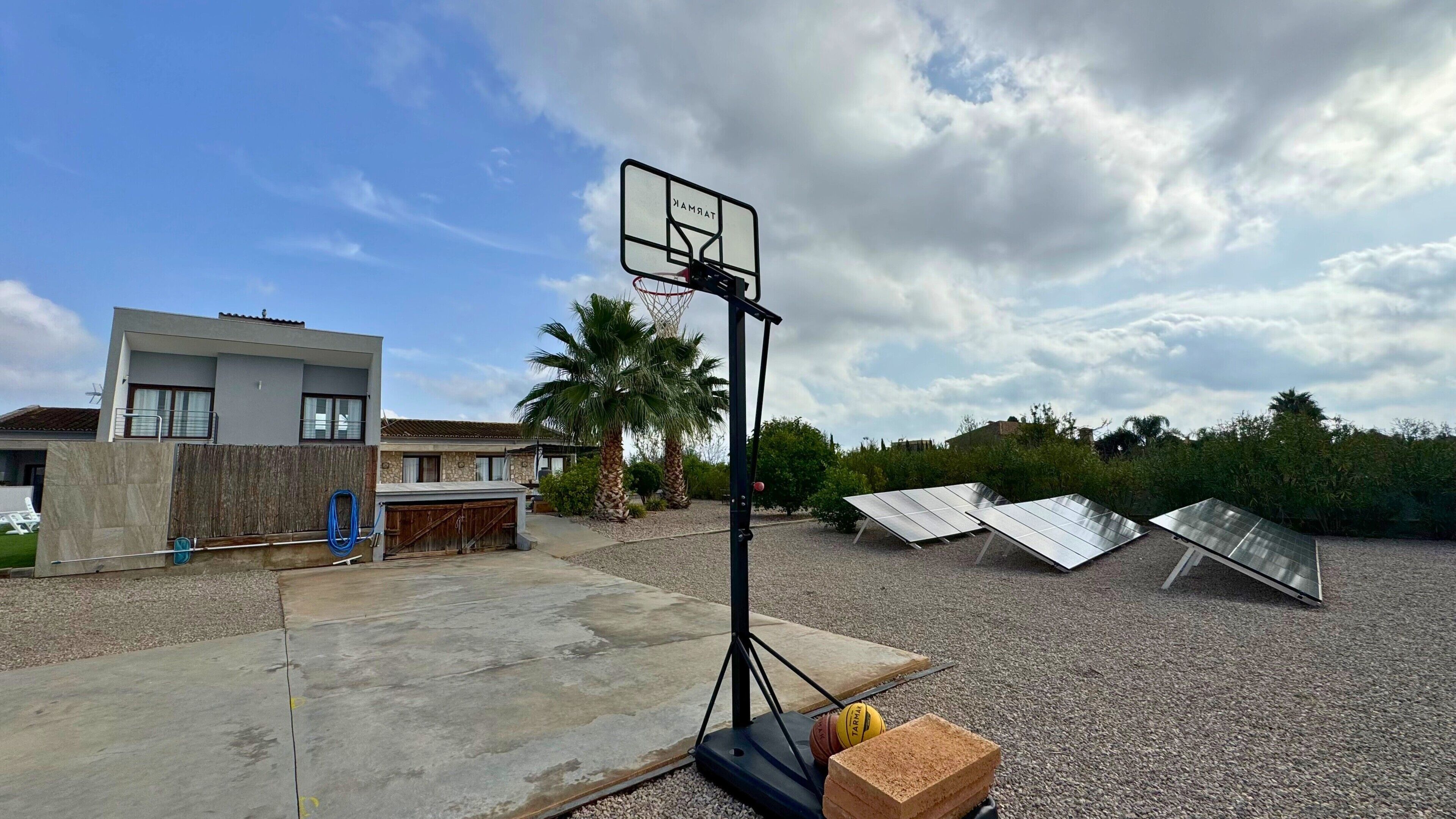 Canasta de baloncesto en un patio trasero con paneles solares y una casa moderna al fondo.