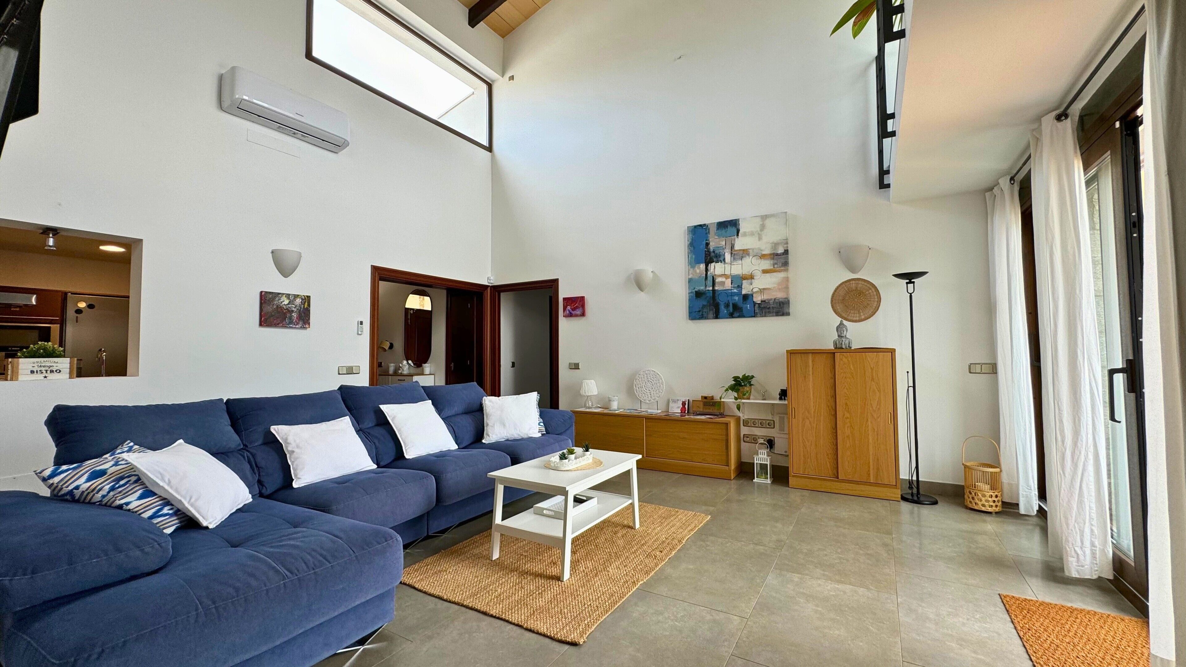 Una sala de estar moderna con un sofá azul, una mesa de centro blanca y una cocina con armarios de madera.