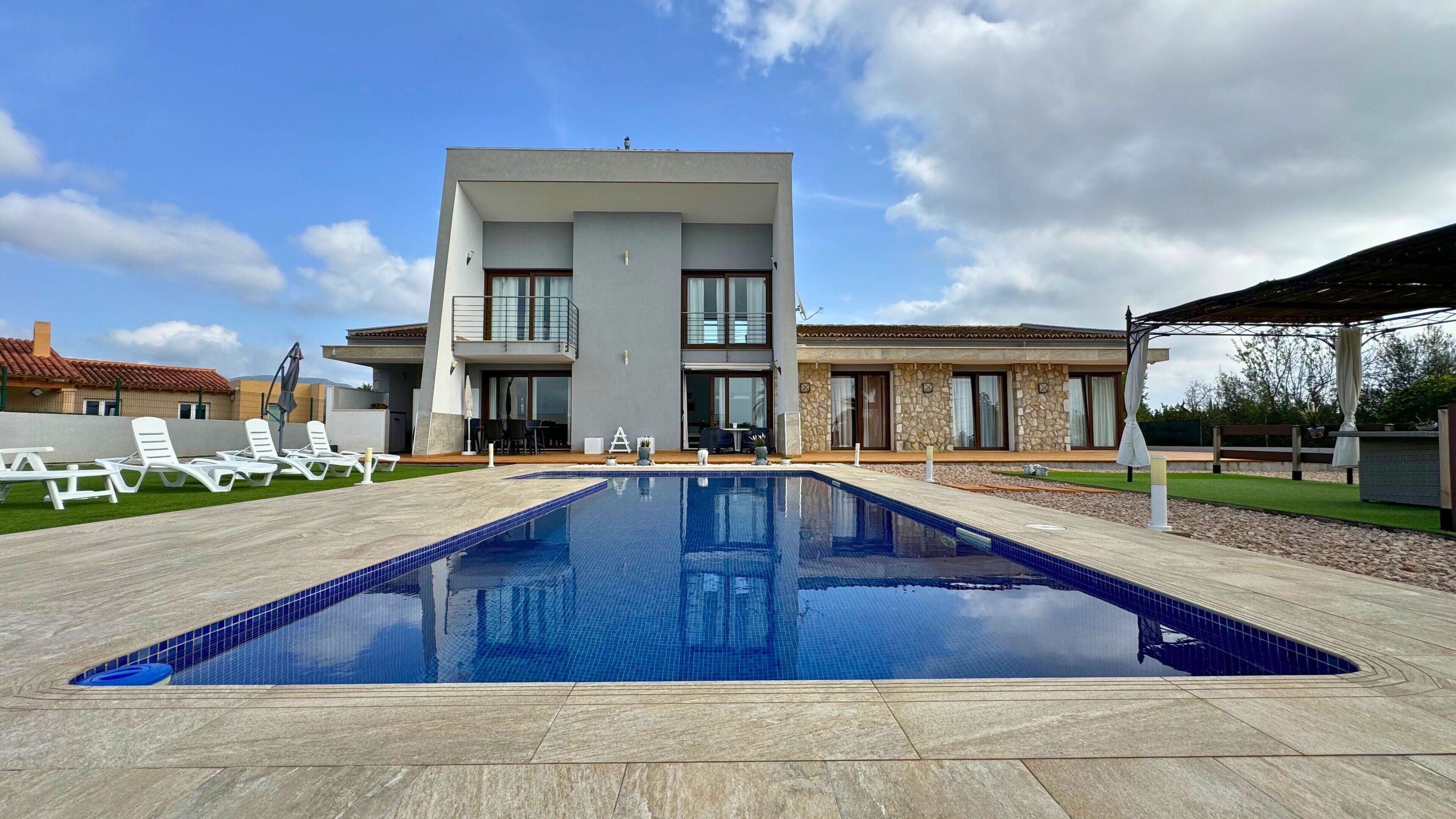Una casa moderna de dos pisos con piscina, mobiliario exterior y fachada de piedra.